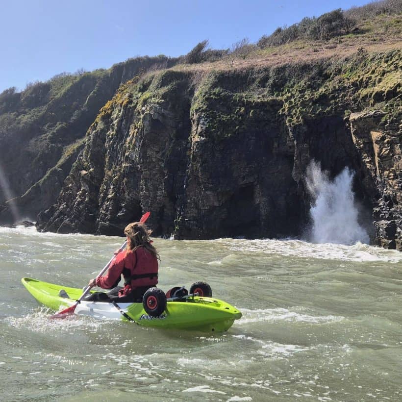 Sea kayaker paddling below the cliffs near Tenby with a wave breaking against the rocks