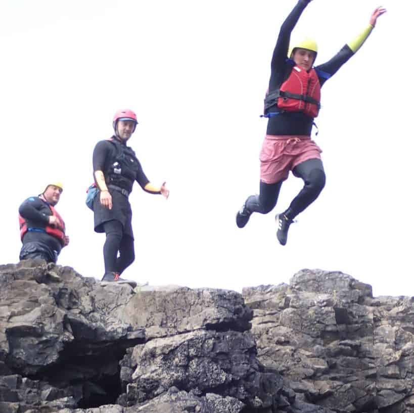 Guest mid-air on an optional coasteering jump in Pembrokeshire, guide standing by